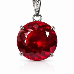 May include: A round, faceted, deep red gemstone pendant set in a four-prong silver-toned metal setting. The pendant features a decorative, textured silver-toned bail at the top, designed to hold a chain for wearing as a necklace.