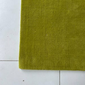 K&ouml;nnte beinhalten: Ein rechteckiger Teppich in einem einfarbigen Chartreuse-Gr&uuml;n mit einer dichten, kurzflorigen Textur. Der Teppich hat gerade, saubere Kanten und eine gleichm&auml;&szlig;ige Oberfl&auml;chenbeschaffenheit, die einen konsistenten, lebendigen Gr&uuml;nton zeigt.