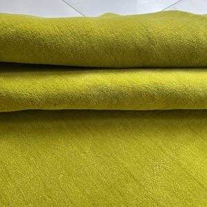 K&ouml;nnte beinhalten: Ein einfarbiger, chartreuse-gr&uuml;ner Textilstoff mit einer dichten, kurzflorigen Textur. Das Material ist umgeschlagen, wodurch zwei deutliche horizontale Schichten entstehen, die die gleichm&auml;&szlig;ige, leuchtende Farbe und die weiche Oberfl&auml;che zeigen.