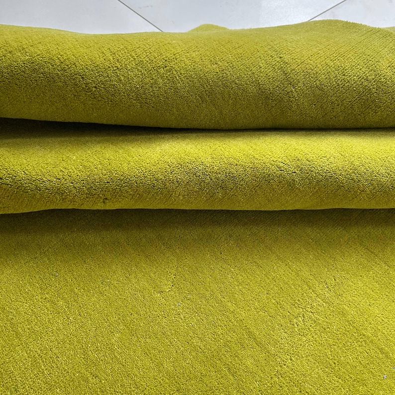 K&ouml;nnte beinhalten: Ein einfarbiger, chartreuse-gr&uuml;ner Textilstoff mit einer dichten, kurzflorigen Textur. Das Material ist umgeschlagen, wodurch zwei deutliche horizontale Schichten entstehen, die die gleichm&auml;&szlig;ige, leuchtende Farbe und die weiche Oberfl&auml;che zeigen.