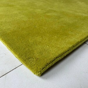 K&ouml;nnte beinhalten: Ein einfarbiger, limettengr&uuml;ner Teppich mit kurzem, dichtem Flor. Der Teppich weist an der Ecke eine saubere, verarbeitete Kante auf, die die gleichm&auml;&szlig;ige Farbe und die konsistente Materialdichte &uuml;ber die gesamte Oberfl&auml;che des Bodenbelags zeigt.