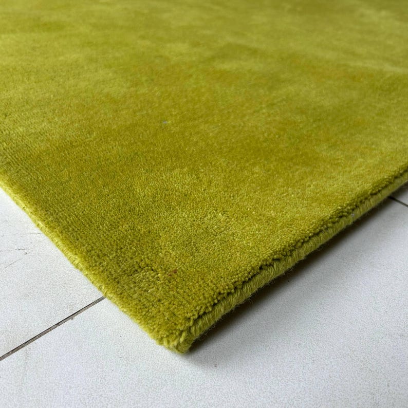 K&ouml;nnte beinhalten: Ein einfarbiger, limettengr&uuml;ner Teppich mit kurzem, dichtem Flor. Der Teppich weist an der Ecke eine saubere, verarbeitete Kante auf, die die gleichm&auml;&szlig;ige Farbe und die konsistente Materialdichte &uuml;ber die gesamte Oberfl&auml;che des Bodenbelags zeigt.