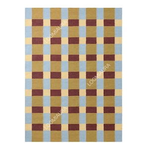 May include: Rectangular woven rug with a checkered pattern. The rug features alternating squares of light blue, tan, olive green, and burgundy. The text "LOOMIAURA" is printed vertically on the rug.