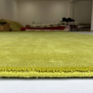 K&ouml;nnte beinhalten: Ein lindgr&uuml;ner Teppich mit einer kurzen, dichten Florstruktur. Der Teppich weist an der unteren Kante einen fertig vern&auml;hten Rand auf, der die Dicke des Materials sowie die gleichm&auml;&szlig;ige, leuchtend gr&uuml;ne Farbe der gesamten Oberfl&auml;che zeigt.