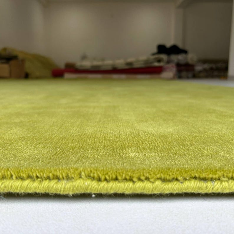 K&ouml;nnte beinhalten: Ein lindgr&uuml;ner Teppich mit einer kurzen, dichten Florstruktur. Der Teppich weist an der unteren Kante einen fertig vern&auml;hten Rand auf, der die Dicke des Materials sowie die gleichm&auml;&szlig;ige, leuchtend gr&uuml;ne Farbe der gesamten Oberfl&auml;che zeigt.