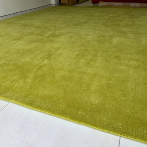 K&ouml;nnte beinhalten: Ein gro&szlig;er, rechteckiger Teppich in einem kr&auml;ftigen, einfarbigen Chartreuse-Gr&uuml;n. Der Teppich weist eine dichte Kurzflor-Struktur mit einem dezenten Glanz auf, der das Licht einf&auml;ngt und leichte Variationen auf der gr&uuml;nen Oberfl&auml;che erzeugt.