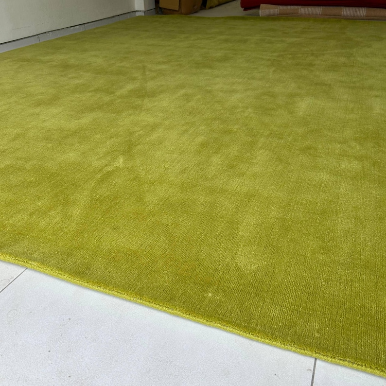 K&ouml;nnte beinhalten: Ein gro&szlig;er, rechteckiger Teppich in einem kr&auml;ftigen, einfarbigen Chartreuse-Gr&uuml;n. Der Teppich weist eine dichte Kurzflor-Struktur mit einem dezenten Glanz auf, der das Licht einf&auml;ngt und leichte Variationen auf der gr&uuml;nen Oberfl&auml;che erzeugt.