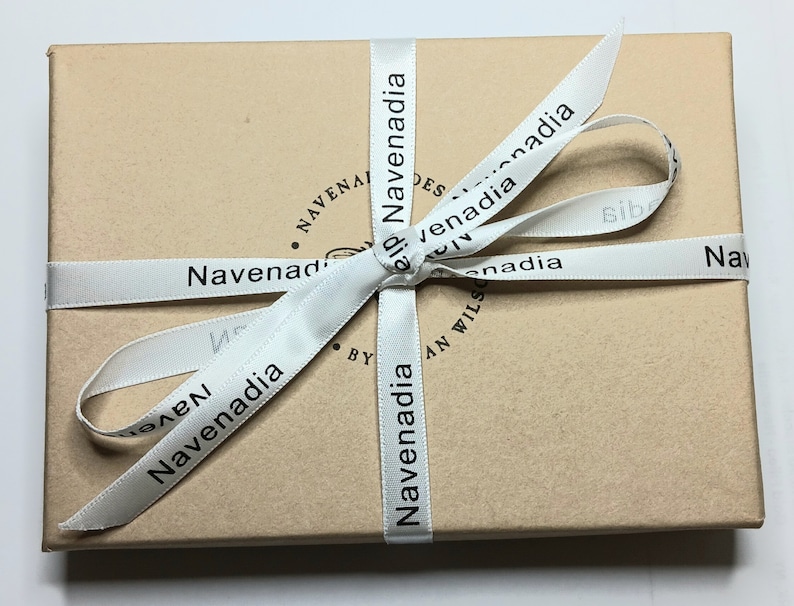 May include: A brown cardboard box with a white ribbon tied in a bow. The ribbon has the text "Navenadia" printed on it.