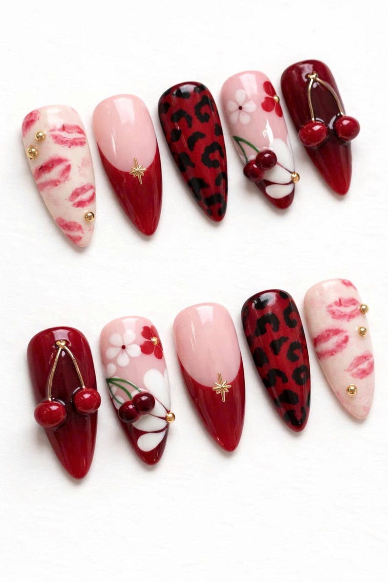 May include: A set of ten almond-shaped artificial nails with various designs. The designs include red leopard print, pink and red cherry accents, pink and white floral patterns, and pink with red tips. Some nails feature gold star or stud embellishments.