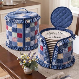May include: Two round, quilted fabric plate storage cases featuring a blue-toned patchwork pattern with ruffled trim. One case is closed with a zipper, while the other is open, revealing a stack of white plates with the text Marifetli İşler Inci Akman.