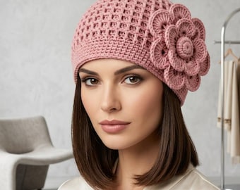 May include: A dusty rose crochet hat with a large, three-dimensional flower on the side. The hat has an open, lattice-like weave. The flower is made of layered, circular petals. The hat is a soft, feminine accessory.