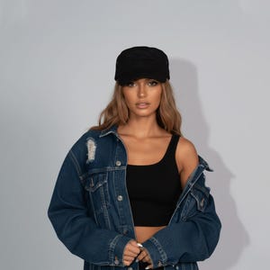 Op de afbeelding: Zwarte pet in militaire stijl met een platte klep. De pet wordt gedragen met een donkerblauwe spijkerjas met distressed details en een zwarte tanktop. De achtergrond is effen lichtgrijs.