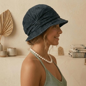 May include: A dark denim cloche hat with a gathered crown and a small brim. The hat is a deep indigo color and appears to be made of a soft fabric. The hat is a stylish accessory.
