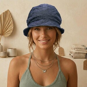May include: A blue denim bucket hat with a slightly distressed appearance. The hat has a rounded crown and a short brim. The person is wearing a layered silver necklace with a butterfly pendant. The person is wearing a green halter top.