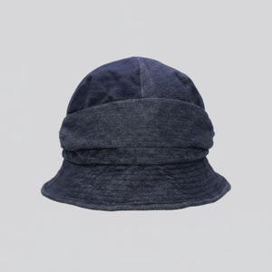 May include: A dark blue denim bucket hat. The hat features a wide, folded brim and a rounded crown. The denim fabric has a slightly faded appearance, giving it a casual, worn look. The hat is designed for sun protection and style.