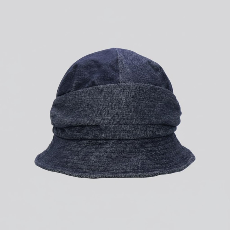 May include: A dark blue denim bucket hat. The hat features a wide, folded brim and a rounded crown. The denim fabric has a slightly faded appearance, giving it a casual, worn look. The hat is designed for sun protection and style.