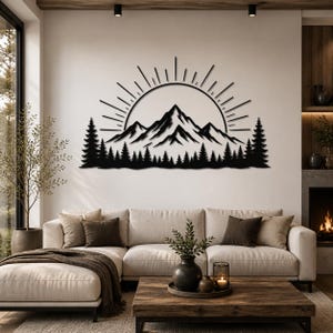 May include: Black metal wall art depicting a mountain range with a rising sun and a forest silhouette. The artwork is mounted on a white wall above a beige sofa, creating a nature-inspired home decor theme.
