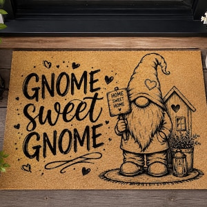 Könnte beinhalten: Eine rechteckige, beigefarbene Fußmatte aus Kokosfaser mit einem schwarzen Aufdruck eines Gnoms, der ein Schild mit der Aufschrift "HOME SWEET HOME" hält. Der Text "GNOME sweet GNOME" ist in großen schwarzen Buchstaben abgebildet.