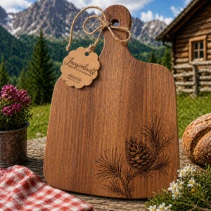Könnte beinhalten: Ein Holzschneidebrett mit Griff und dekorativem Tannenzapfen-Design. Das Brett hat ein Etikett mit der Aufschrift "Jausenbrett" und "alpverde". Das Brett ist mit Bindfaden gebunden und befindet sich im Freien.