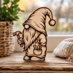 May include: Wooden gnome figurine with a long beard, holding a hammer. The gnome wears a hat with a pom-pom and has a pocket with tools. The wood has a natural grain and is laser-cut.