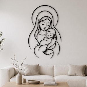 May include: A black metal wall art piece depicting a mother holding a baby. The artwork features a minimalist line drawing style, with the figures outlined against a white wall. The mother is wearing a head covering.