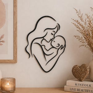 Puede incluir: Arte de pared de metal negro que representa a una madre besando a un bebé. La obra de arte presenta un diseño minimalista con líneas fluidas, creando una silueta de las figuras. La pieza está montada en una pared de color neutro.