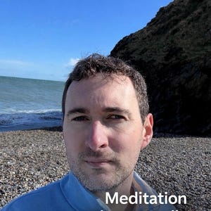 Puede incluir: Una persona con una chaqueta azul claro con el texto "Meditation That Actually Works For You" en blanco. El fondo muestra una playa con costa rocosa, el océano y una colina bajo un cielo azul.