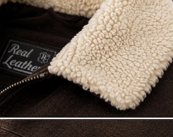 Puede incluir: Primer plano de una chaqueta de ante marrón con cuello de borrego color crema. La chaqueta tiene cierre de cremallera y una etiqueta que dice "Real Leather". Se aprecia la textura del ante.