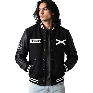 May include: A black varsity jacket with long black sleeves, a snap-button front, and white striped ribbed trim on the collar, cuffs, and hem. The chest features a white Roman numeral MMXIV patch and a white X patch, with a circular R logo on the sleeve.