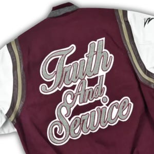 May include: Maroon varsity jacket with white sleeves and the words "Truth And Service" in a silver script. The jacket has a gray collar and gold stripes on the sleeves. A black logo is visible on the left sleeve.
