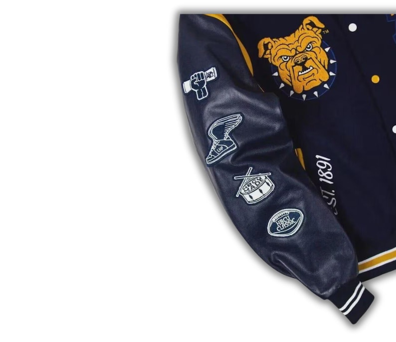 Pode incluir: Um casaco varsity azul-marinho com punhos canelados &agrave;s riscas amarelas e brancas. A manga apresenta emblemas bordados a branco de um punho, um t&eacute;nis alado, um tambor e uma bola de futebol americano. O peito exibe uma cabe&ccedil;a de bulldog amarela e o texto EST. 1891.