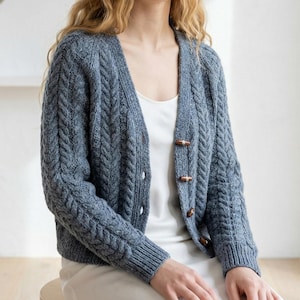 Könnte beinhalten: Ein Set aus drei Keramikbechern mit gesprenkelter, matter Oberfläche. Die Becher sind in Creme-, Hellgrau- und Dunkelgrautönen gehalten. Jeder Becher hat ein schlichtes, minimalistisches Design und einen abgerundeten Henkel.