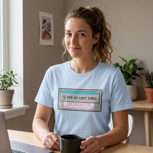 May include: Light blue t-shirt with the text "PER MY LAST EMAIL" displayed in a retro computer window design. The shirt is made of a soft material and is suitable for casual wear. The person is holding a black mug.