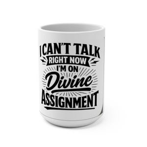 Könnte beinhalten: Weiße Keramik-Tasse mit dem schwarzen Text "I CAN'T TALK RIGHT NOW I'M ON Divine ASSIGNMENT". Die Tasse hat eine geschwungene Form und einen großen Henkel. Der Text ist in einer fetten, stilisierten Schrift.