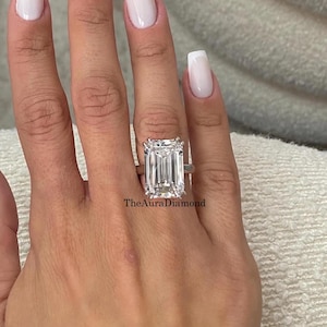 May include: A large emerald-cut diamond ring with a silver band. The ring is the focal point, set against a background of a hand with white nail polish. The Aura Diamond is visible on the ring.