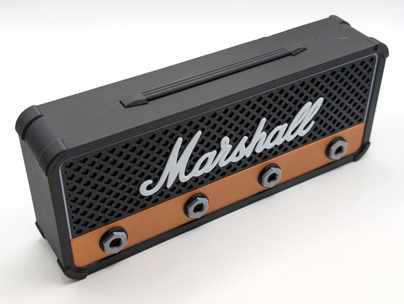 May include: Black and copper-colored miniature amplifier with the word "Marshall" in white script across the front. The amplifier has a handle on top and three black knobs. The front has a speaker grill design.