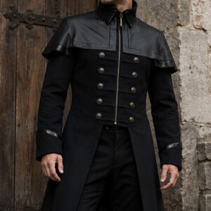 Peut inclure: Long manteau noir avec une cape d'épaule en similicuir et des boutons dorés. Le manteau a un col montant et une fermeture éclair. Les manches ont des accents en similicuir. Le manteau est porté avec un pantalon noir.