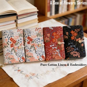 May include: Four floral embroidered book covers in the "A Sea of Flowers Series" are displayed. The covers feature various floral patterns in red, orange, blue, and white, with wooden button closures. The text "Pure Cotton Linen & Embroidery" is visible.