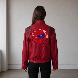 Könnte beinhalten: Rote Lederjacke mit einem runden Aufnäher auf dem Rücken. Der Aufnäher zeigt eine rote und blaue Pillen-Grafik mit den Worten "GOOD FOR HEALTH" und "BAD FOR EDUCATION" in einem kreisförmigen Muster.