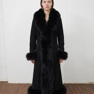 May include: A long, black coat featuring a fur collar, cuffs, and trim. The coat is made from a dark, suede-like fabric and has a classic, elegant design. The fur trim adds a touch of luxury to the garment, creating a sophisticated look.
