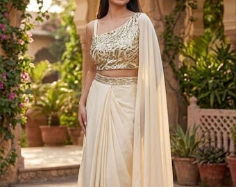 May include: An ivory-colored formal outfit featuring a one-shoulder top with gold embroidery, a matching draped skirt, and a flowing shawl. The ensemble is suitable for special occasions.