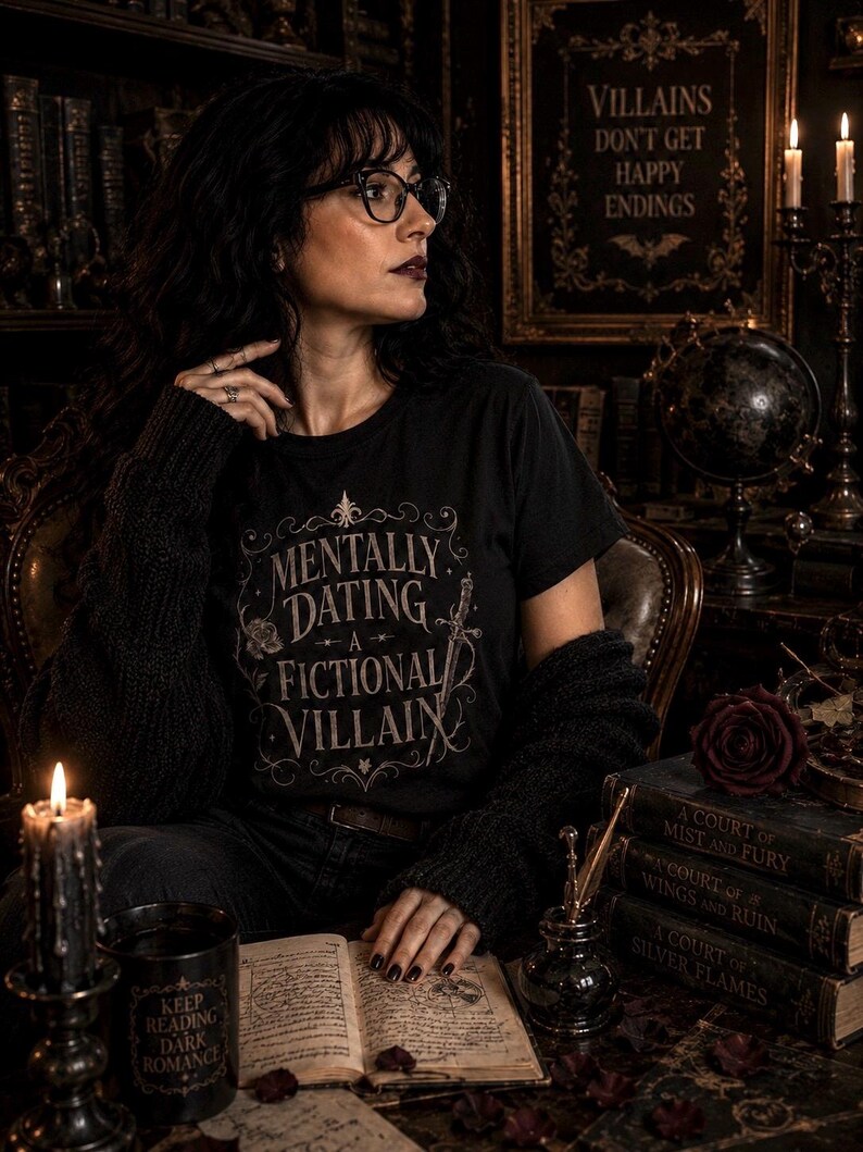 Puede incluir: Una persona con una camiseta negra con la frase "MENTALLY DATING A FICTIONAL VILLAIN" est&aacute; en una habitaci&oacute;n oscura. Se ven libros, velas y un letrero que dice "VILLAINS DON'T GET HAPPY ENDINGS".