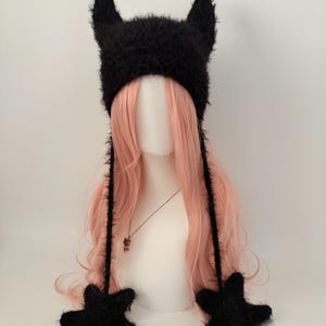 May include: A black, fuzzy hat with two pointed horns and star-shaped ear flaps. The hat is made of a soft, textured material and is designed to be worn on the head. The hat is a unique and stylish accessory.