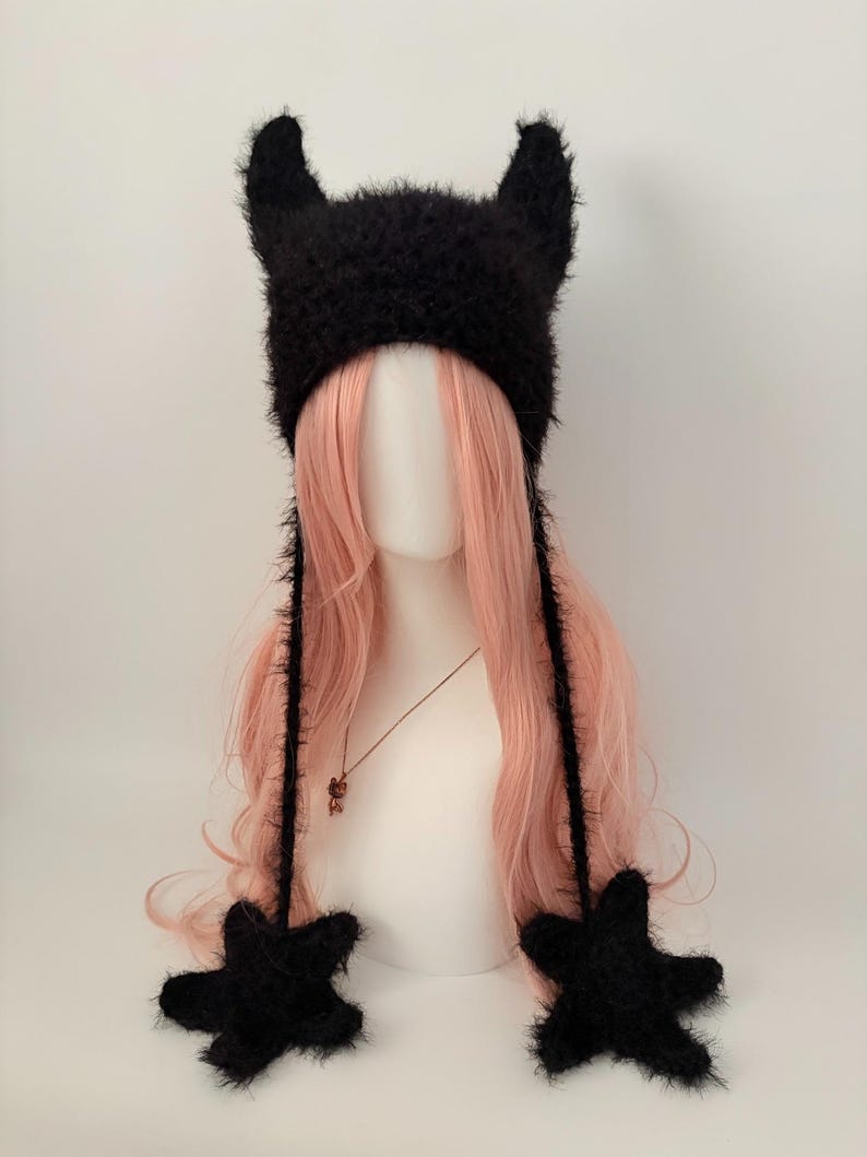 May include: A black, fuzzy hat with two pointed horns and star-shaped ear flaps. The hat is made of a soft, textured material and is designed to be worn on the head. The hat is a unique and stylish accessory.