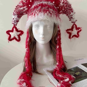 May include: A red and white fuzzy jester-style hat with two long, pointed side extensions. Each extension features a dangling star-shaped ornament at the end. The hat is crafted from a textured, yarn-like material with small white star accents.