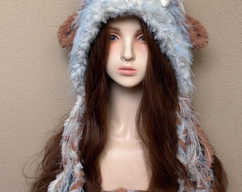 May include: A fuzzy, multi-textured hat featuring a blend of light blue, white, and brown faux fur. The hat includes two rounded brown ears on the sides and long, dangling braided strands of yarn and fur that hang down from the main cap section.