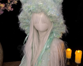 May include: A light mint green faux fur hood featuring pointed cat-like ears and a textured, shaggy finish. The hood is adorned with long, dangling ribbons in matching mint green, including polka-dot patterns and delicate lace trim accents.