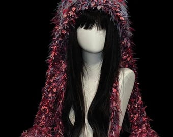May include: A hooded scarf crafted from shaggy, textured yarn in a variegated color palette of deep burgundy, bright red, and soft blue-grey. The long, fringed ends drape down from the hood, featuring a dense, fuzzy construction throughout.