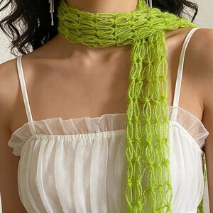 Peut inclure: &Eacute;charpe vert vif en maille ajour&eacute;e port&eacute;e sur une robe blanche. L'&eacute;charpe, d'un vert citron lumineux, contraste avec la robe. La robe a un col &agrave; volants et des bretelles fines.