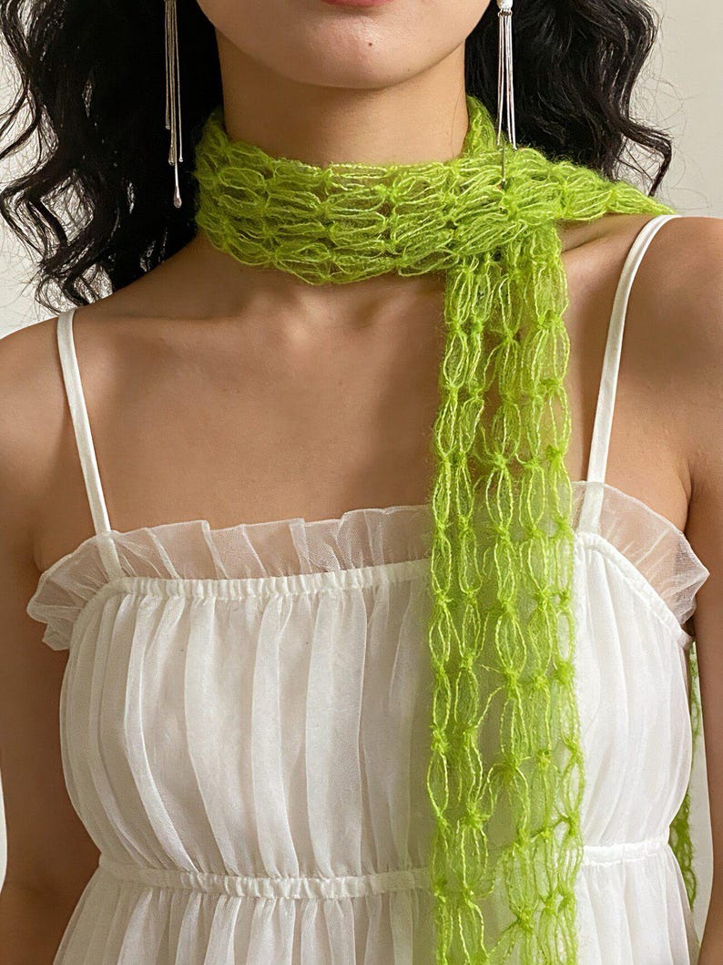 Peut inclure: &Eacute;charpe vert vif en maille ajour&eacute;e port&eacute;e sur une robe blanche. L'&eacute;charpe, d'un vert citron lumineux, contraste avec la robe. La robe a un col &agrave; volants et des bretelles fines.